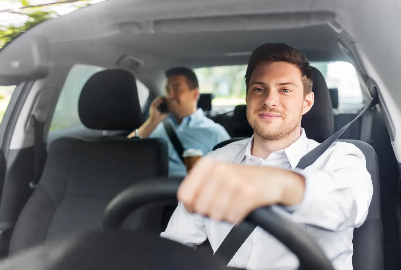 Driver and rear passenger seated in a car, both wearing three-point seat belts.