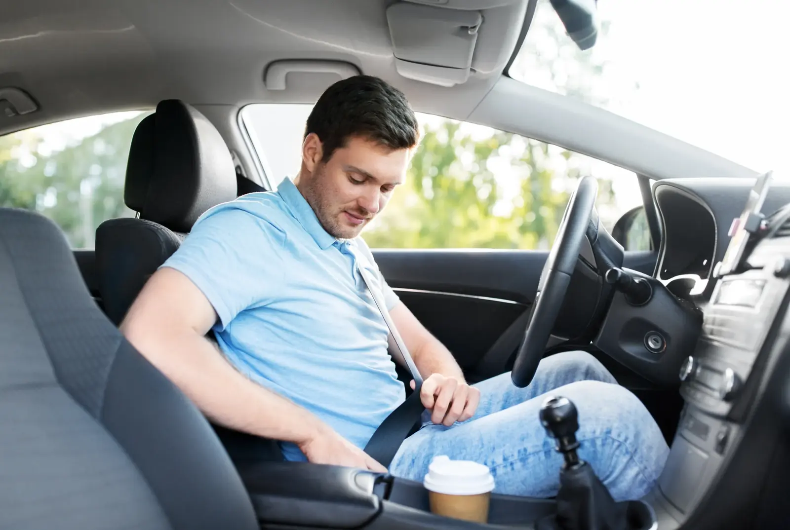 Driver seated in a vehicle cabin fastening the seat belt at the start of a shift.