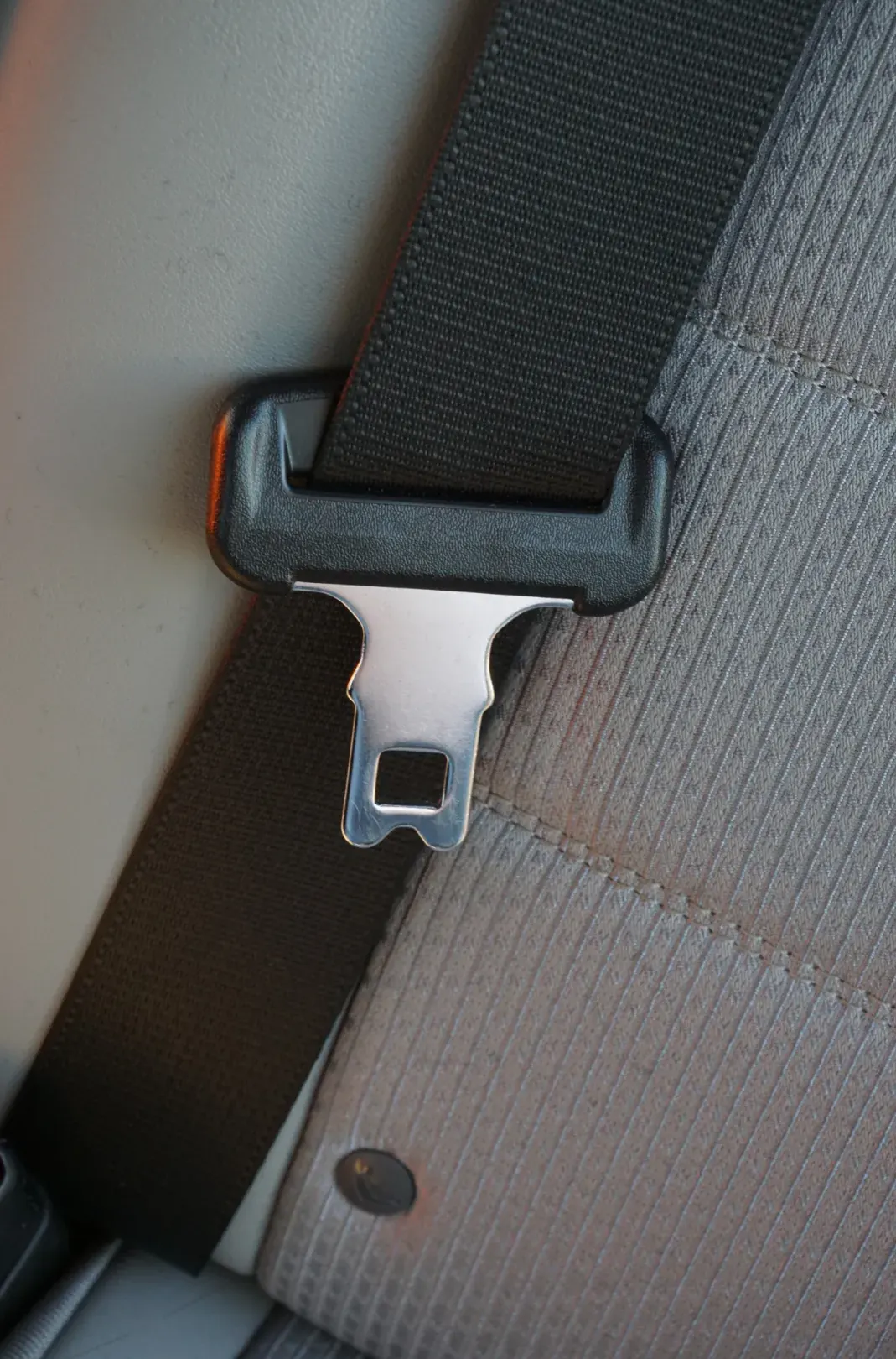 Close-up of a seat belt latch plate resting on woven webbing, showing the weave and edge finish.