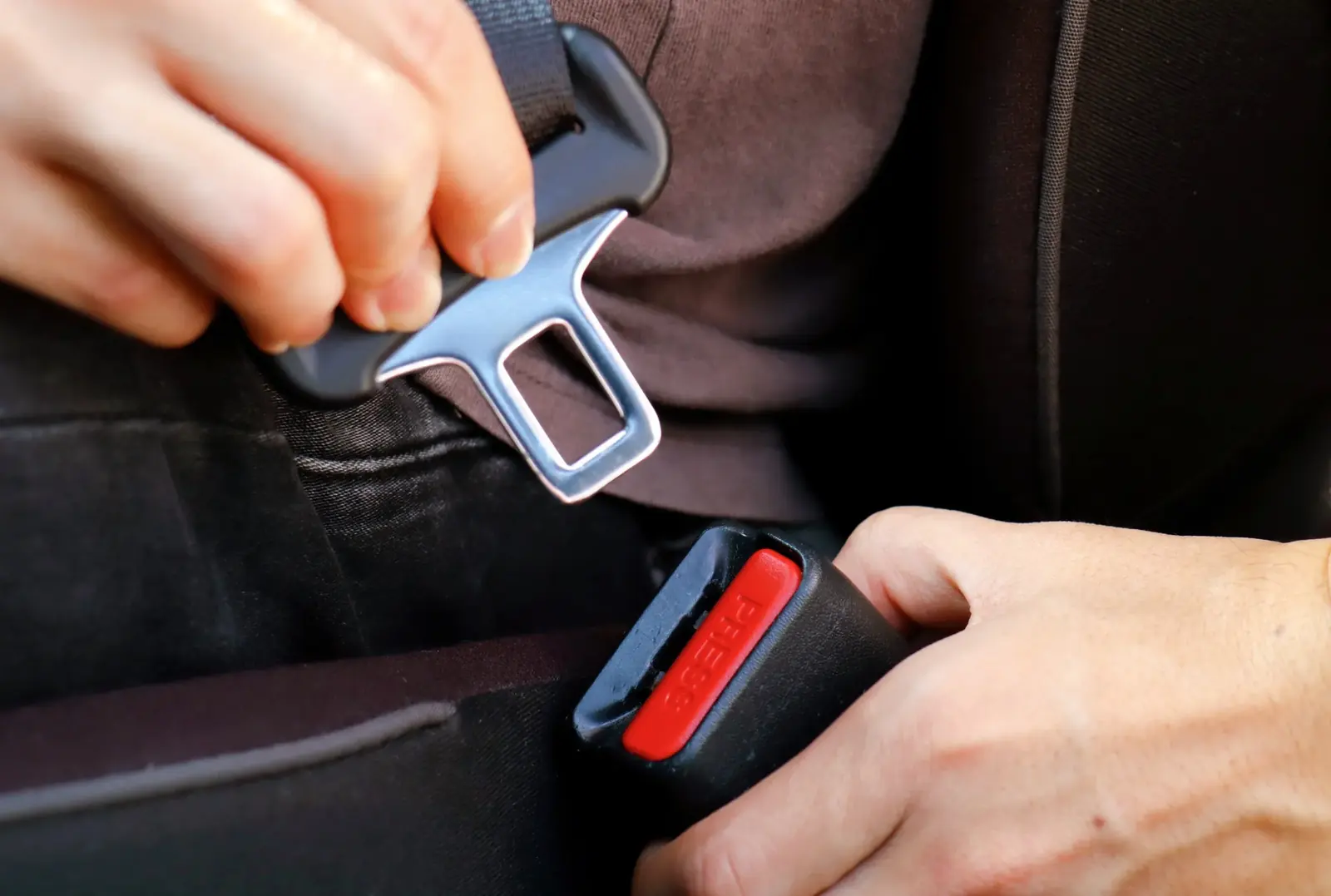 Close view of hands guiding a seat belt tongue into the buckle until it latches.