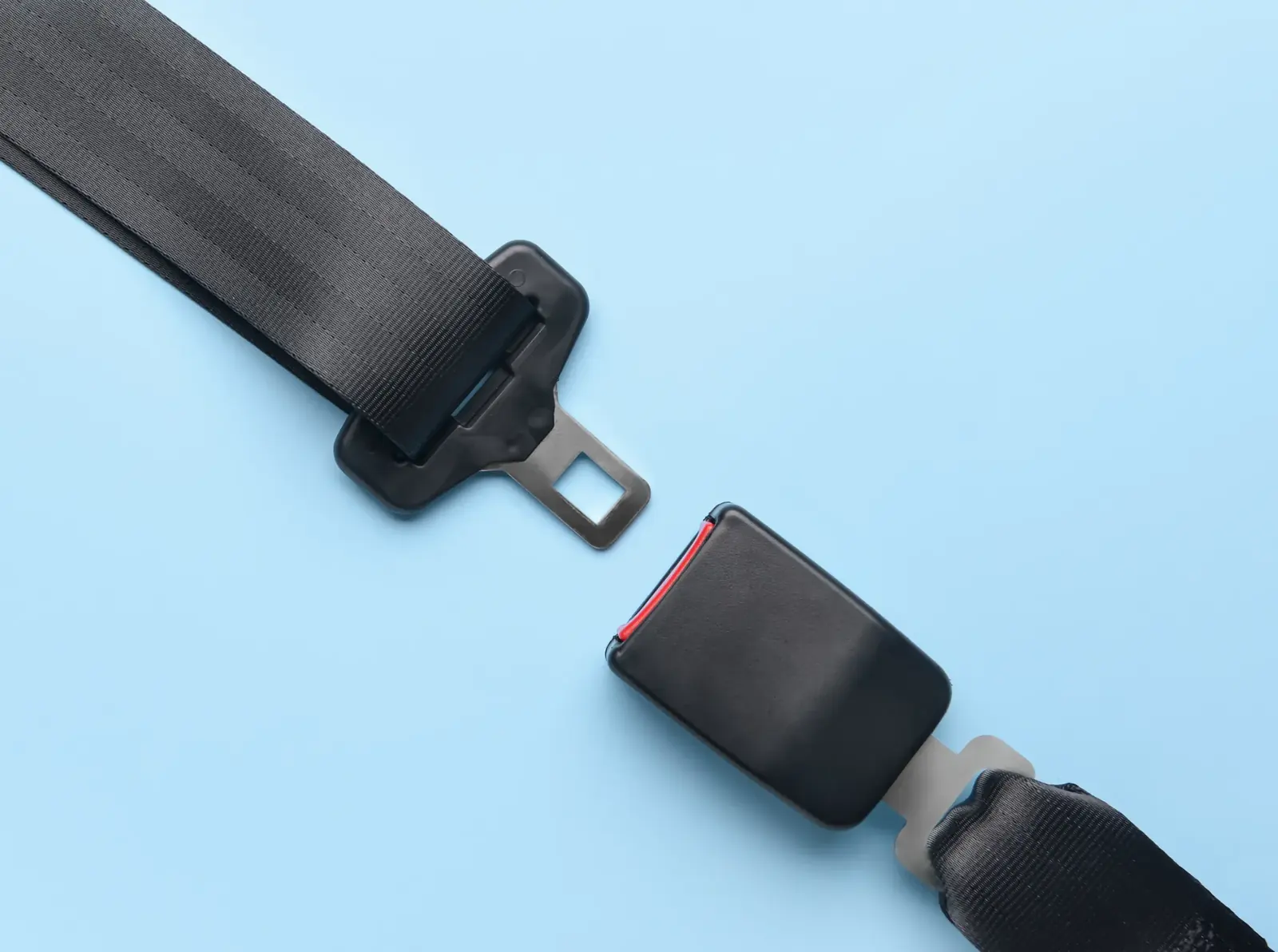 Seat belt tongue and buckle photographed against a plain background, shown just before engagement.