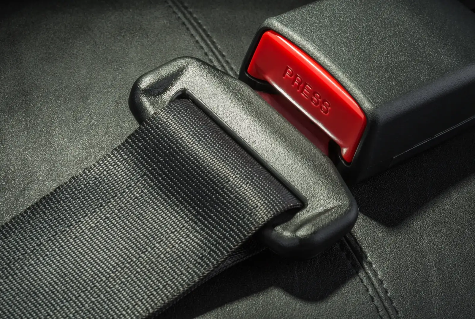 Seat belt buckle with a red release button, shown latched onto webbing.